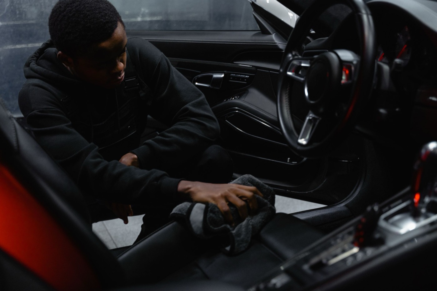 Detailer wiping down the sill and console of a sports car interior with a microfibre towel