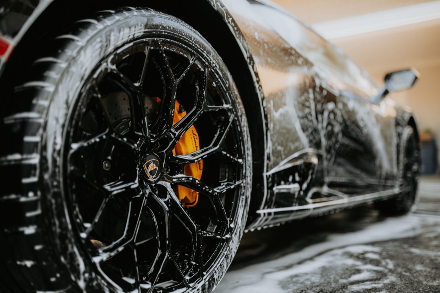 Foam covering a black alloy wheel and the lower body of a sports car