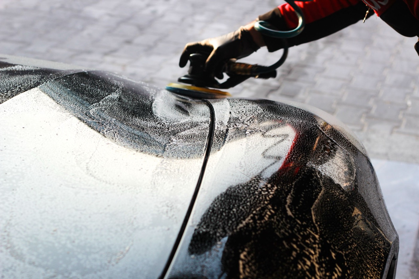 Machine polisher working across a foamed panel on a dark car